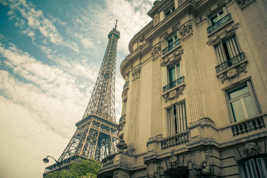 Low angle view of the Eiffel Tower and historic Parisian building against a clear sky, capturing Paris's iconic architecture.
